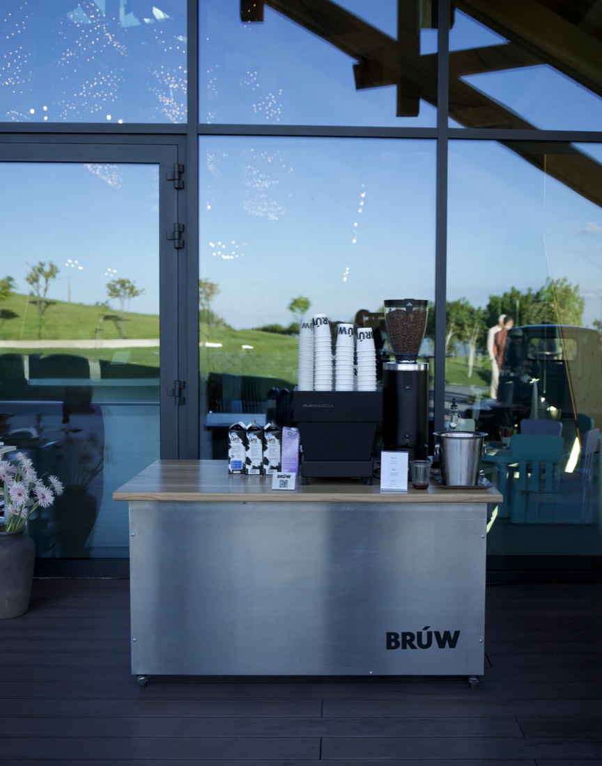 A BRÚW bar set up beside a glass wall, cups stacked and grinder loaded